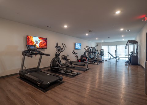a gym with treadmills and other exercise equipment on a wooden floor at The Row on Merchant Apartments, Springdale, Ohio