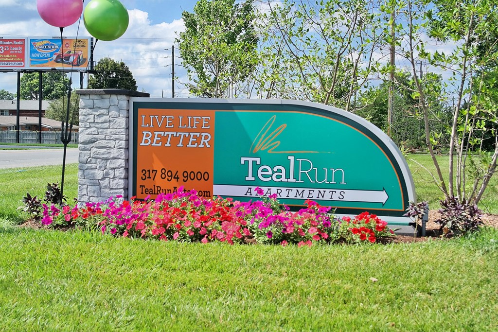 a sign for teal run apartments with flowers and balloons