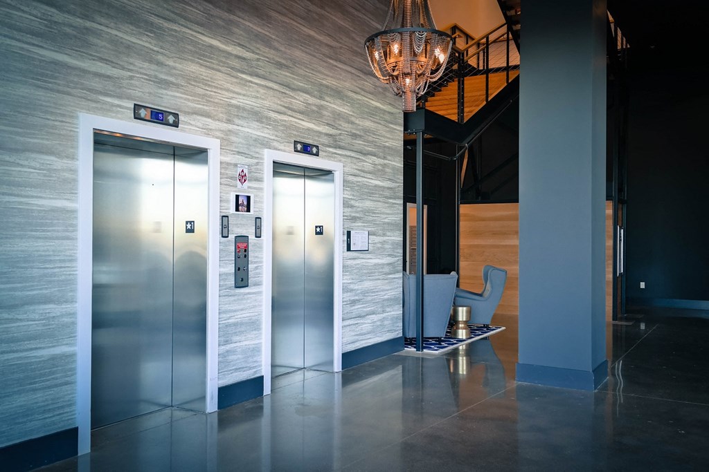 a lobby with three elevators and a chair and a chandelier