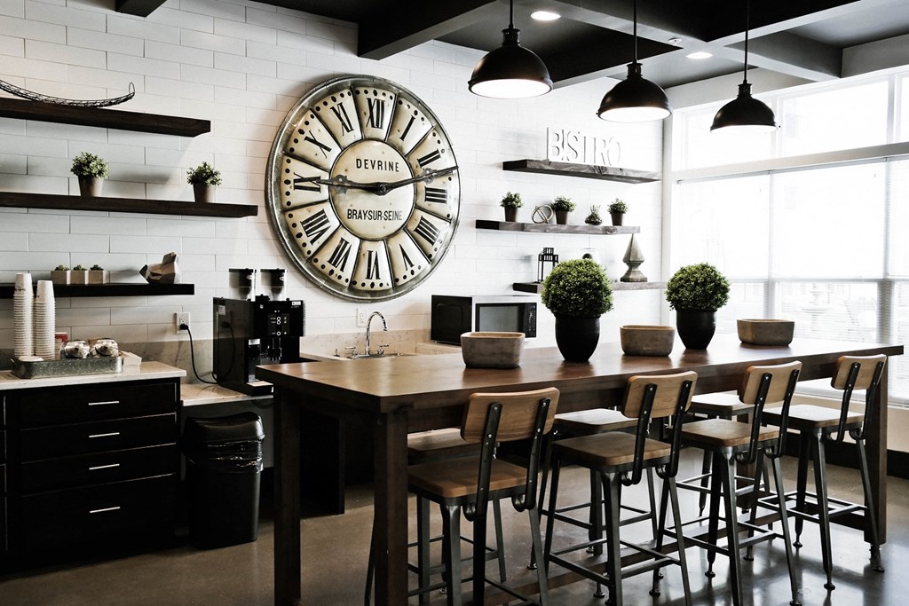 West Chester OH Apartments for Rent - Liberty Center - Community Coffee Bar with Rustic Design, Wooden Stool-Top Table with Chairs, Coffee Station, Storage Shelves, Tile Design, Large Clock, and light