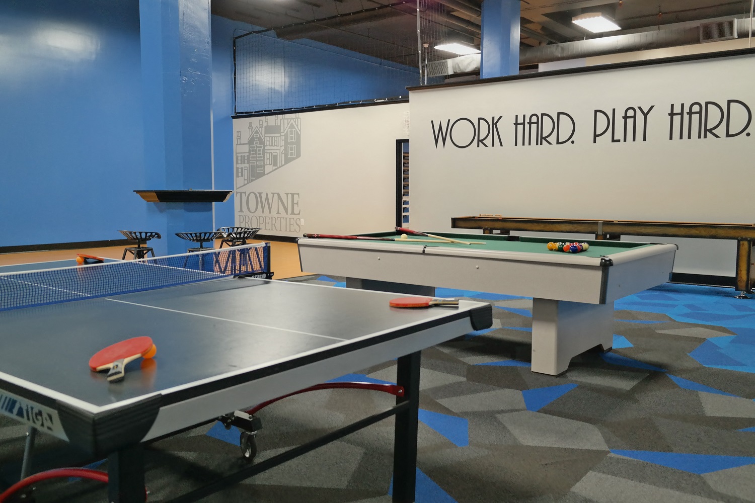 two ping pong tables in a game room with a wall that says work hard