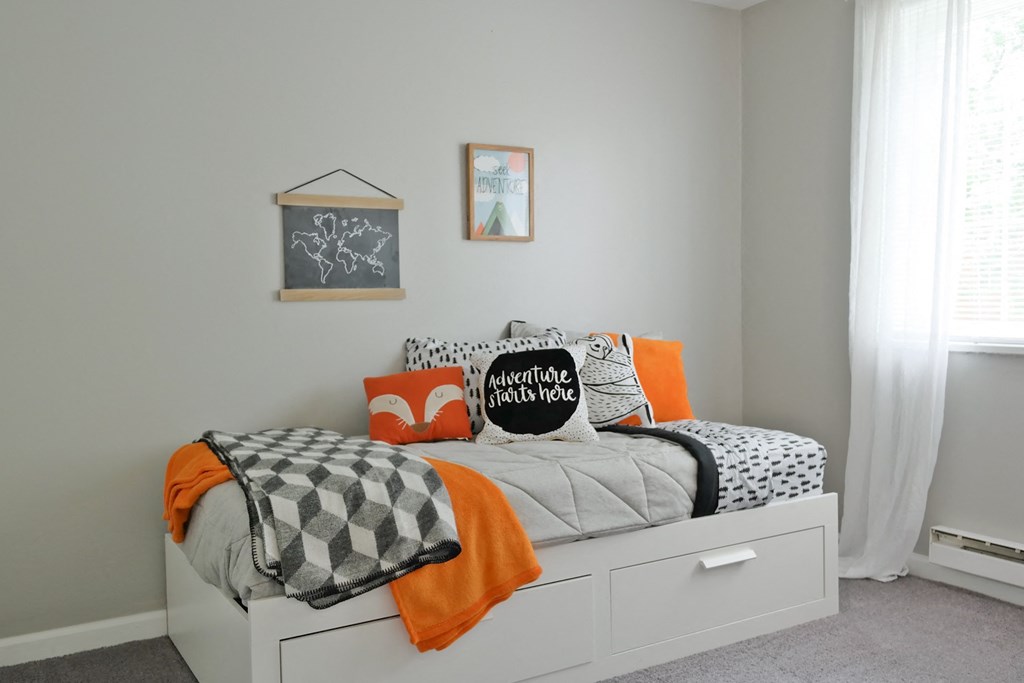 a small bedroom with a bed and orange and black pillows