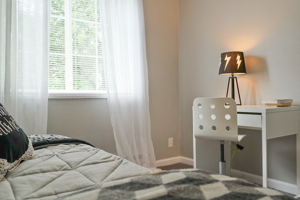 a bedroom with a bed and a desk with a lamp and a window