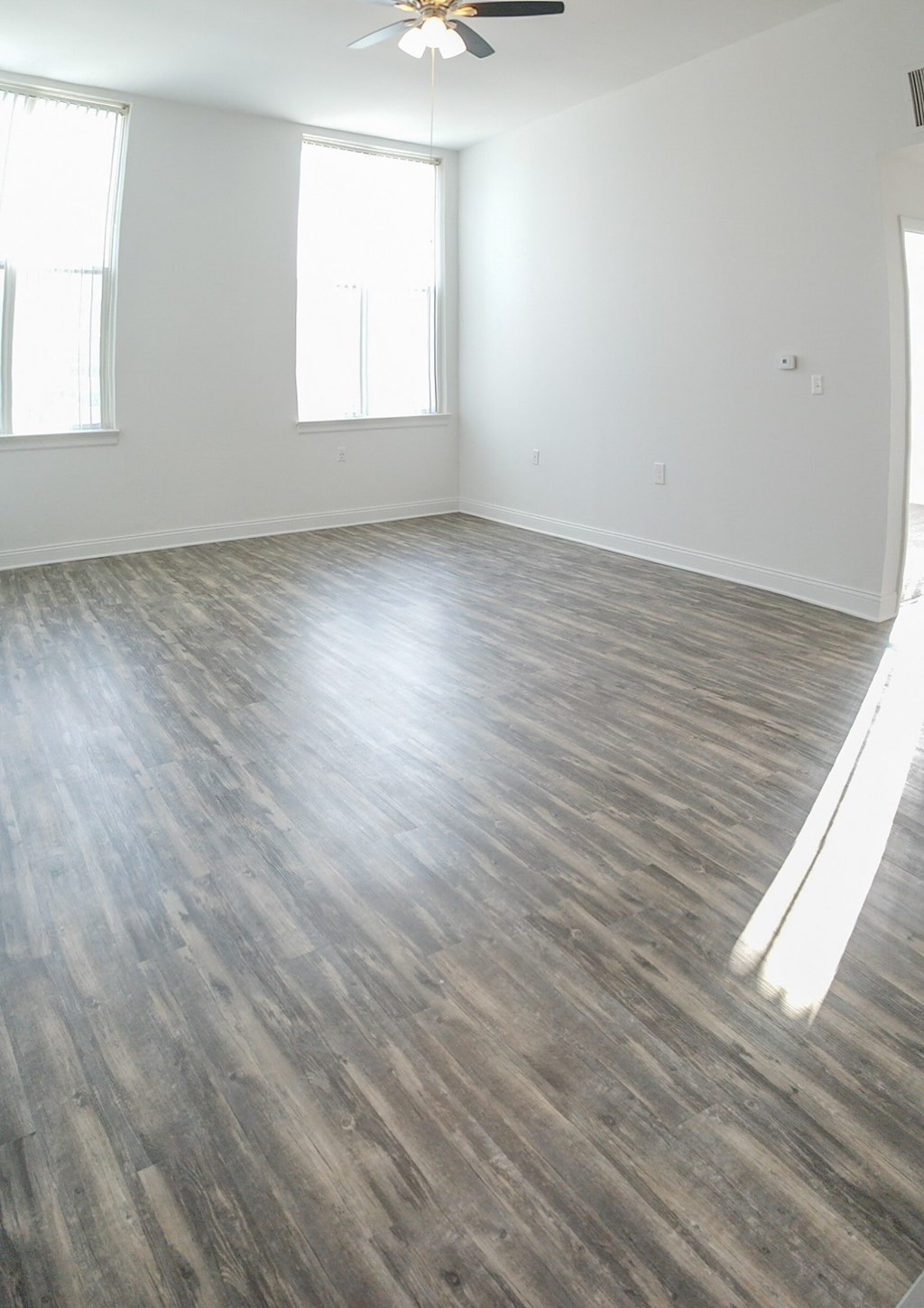 an empty living room with wood floors and a ceiling fan
