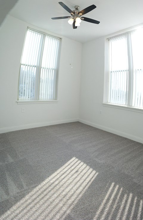 an empty room with a ceiling fan and two windows