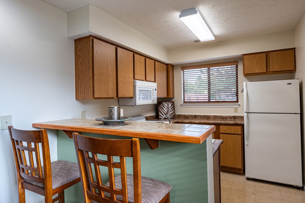 a kitchen with a bar with two chairs and a refrigerator