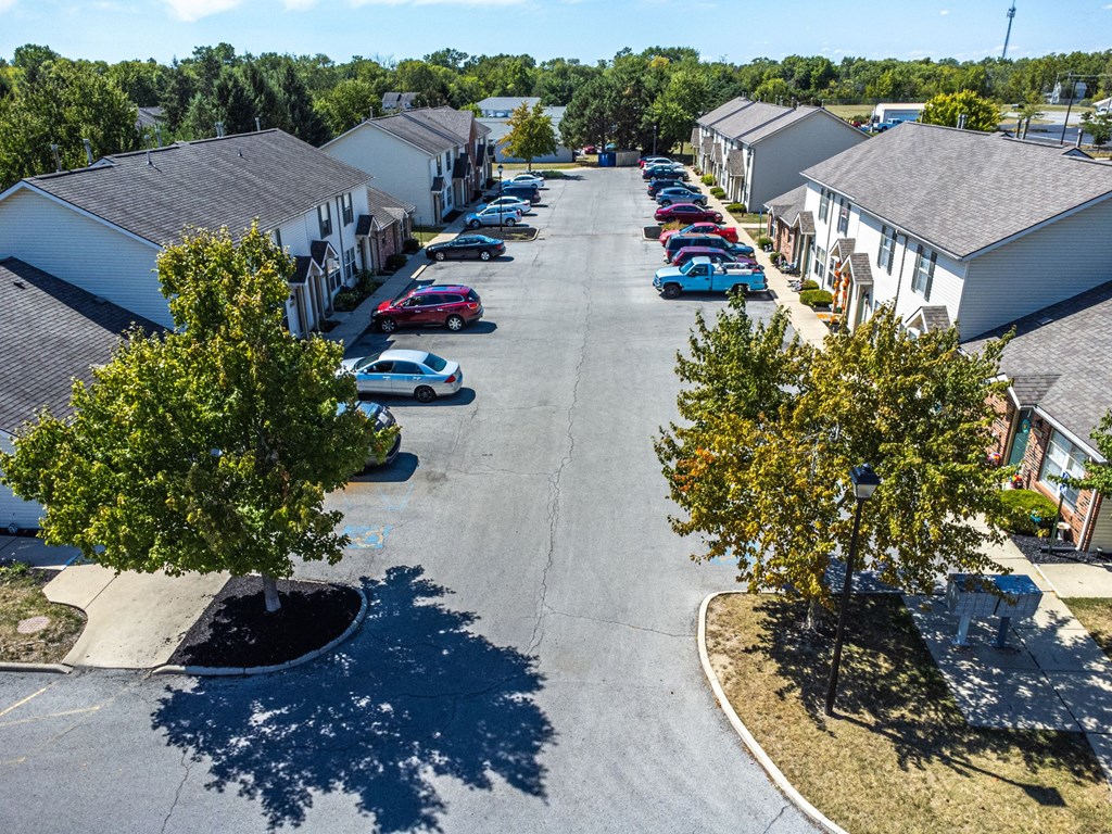 A parking lot with cars and trees in front of apartment buildings.
