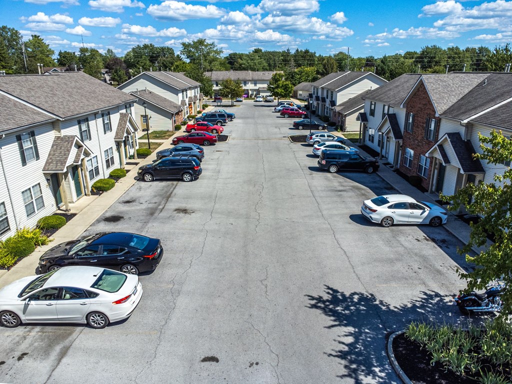 A parking lot with cars and houses in the background.