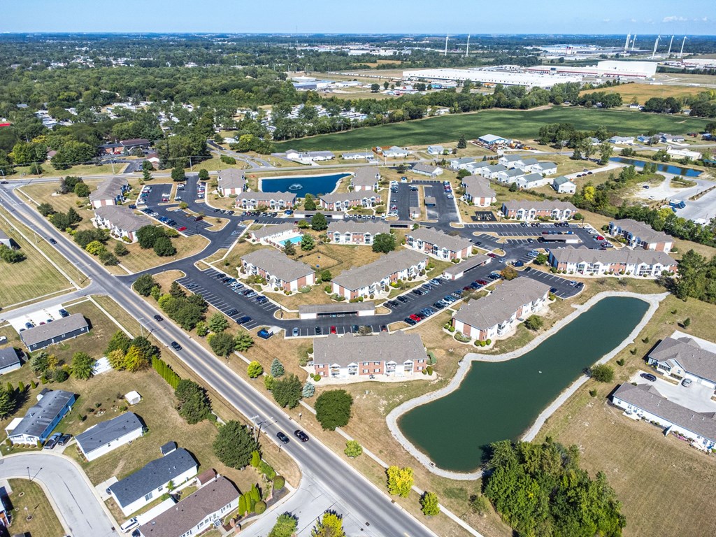 A bird's eye view of a residential area with houses, roads, and a pond.