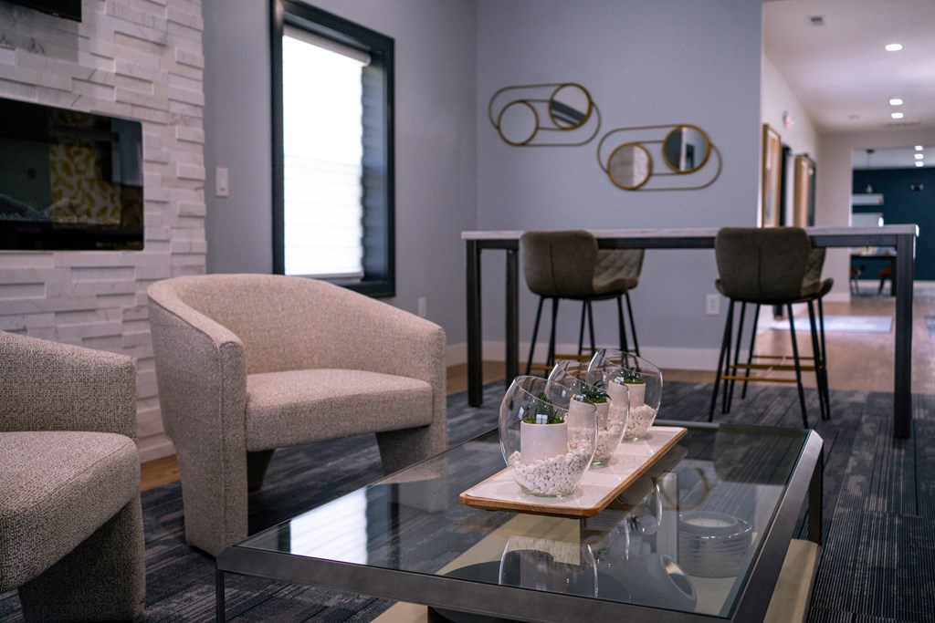 a living room with a glass coffee table and chairs and a kitchen with a bar