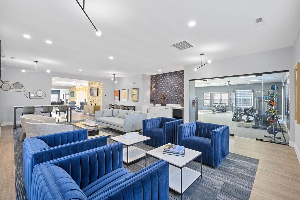 a living room with blue couches and chairs and a kitchen with a glass wall