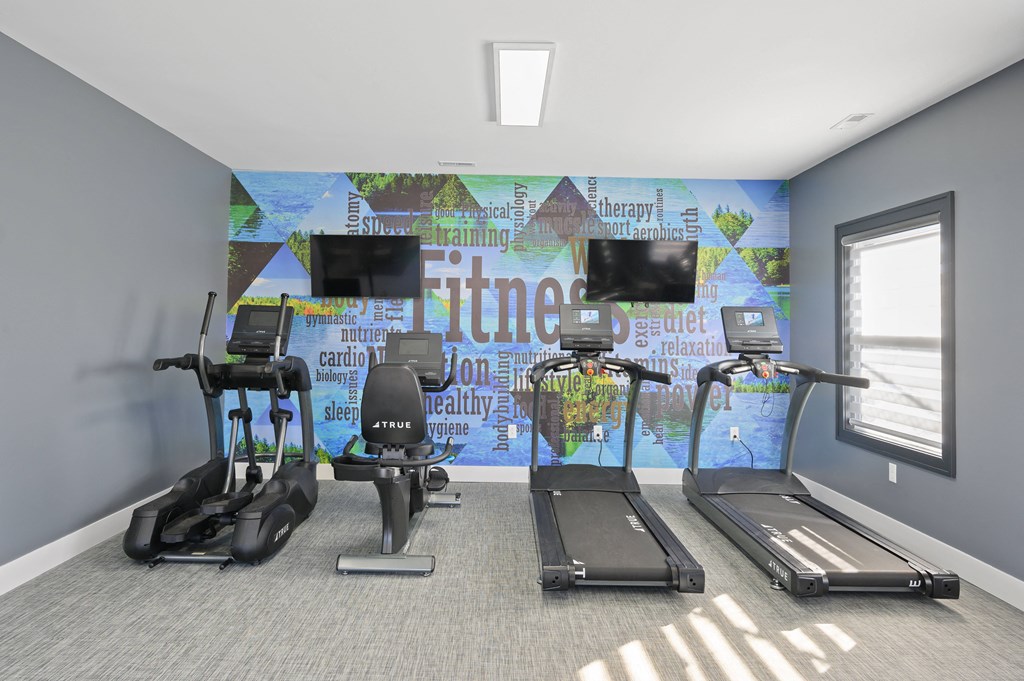 a gym with exercise machines and televisions on the wall