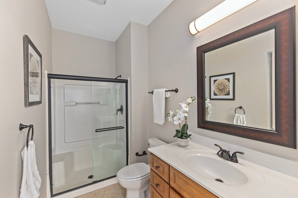 A bathroom with a toilet, sink, mirror and shower.
