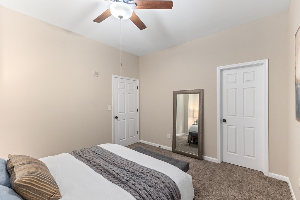 A bedroom with a bed, a ceiling fan, and a mirror.