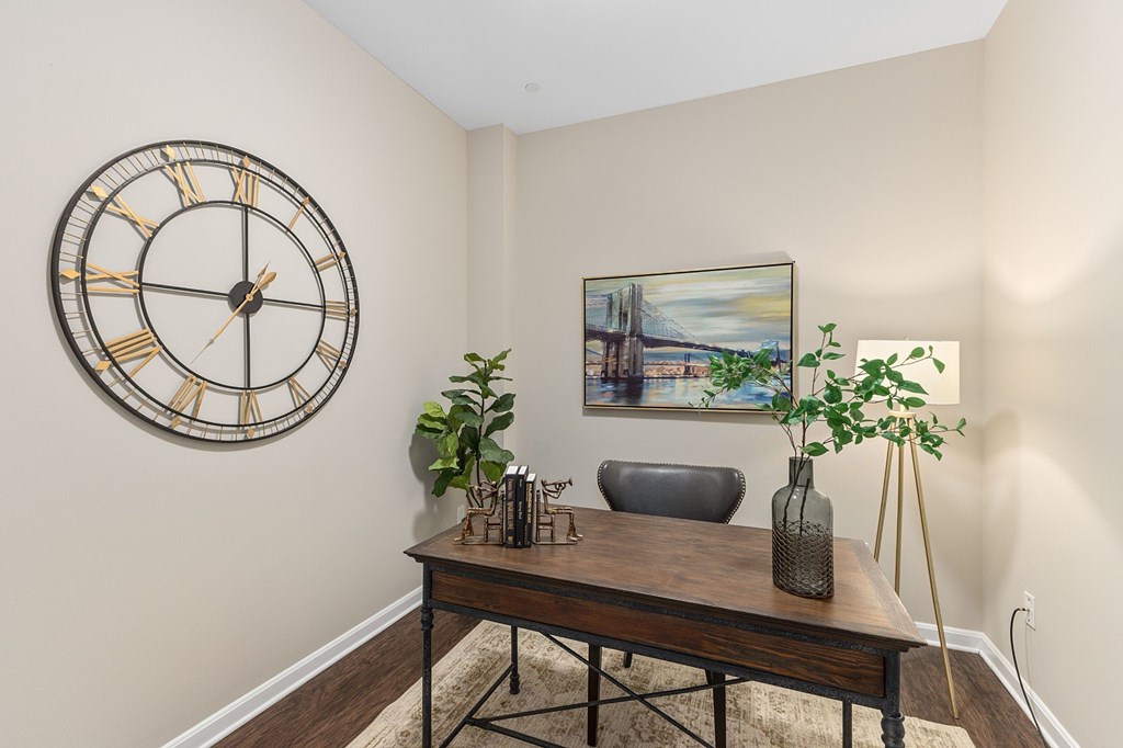 A large clock hangs on the wall above a table with a vase and a plant on it.