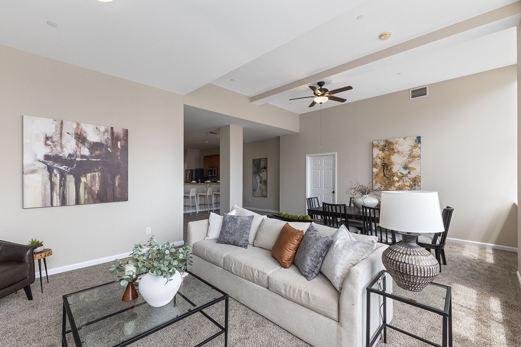 A living room with a white couch, a glass coffee table, and a painting on the wall.