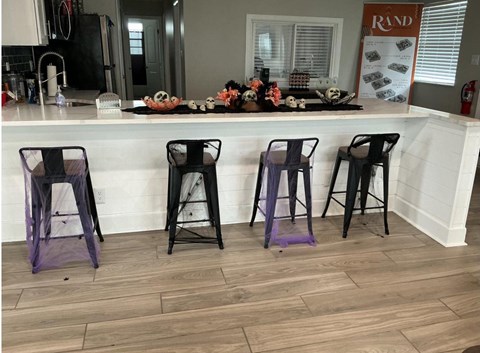 Four black bar stools with purple cushions are placed in front of a bar.