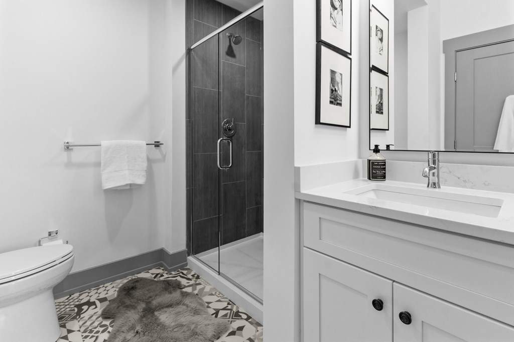 A bathroom with a white toilet, a white sink, a black and white rug, and a black shower stall. at The Ridge Apartments, Ohio