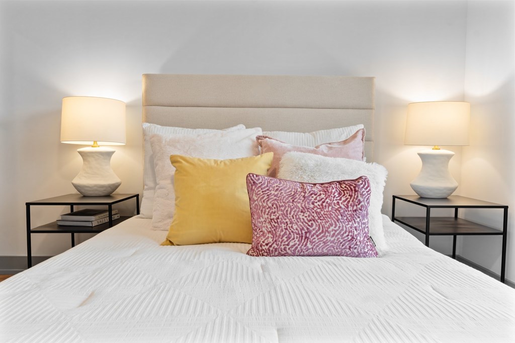 A bed with a white comforter and two pillows with a pink and yellow pillow. at The Ridge Apartments, Cincinnati, OH