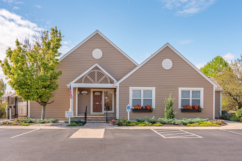 A beige house with a brown door and windows with red flowers.