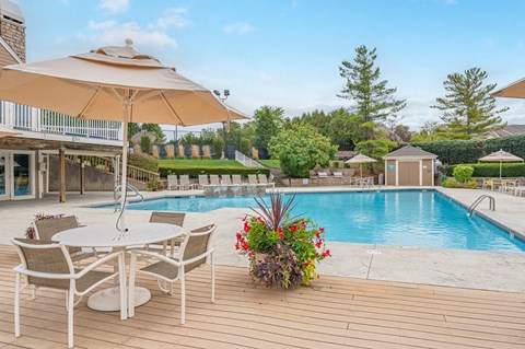 A poolside table with chairs and an umbrella overlooking a pool.