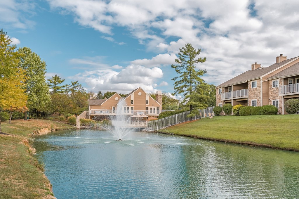A fountain in the middle of a lake in front of a building.