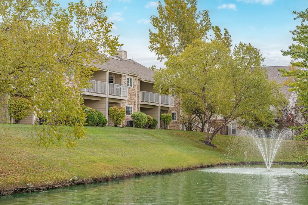 A fountain in the middle of a pond in front of a building.
