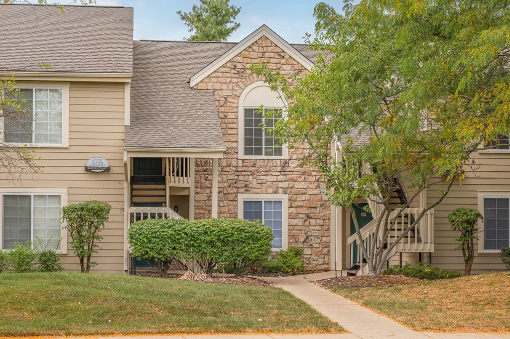 A house with a stone wall and a tree in front.