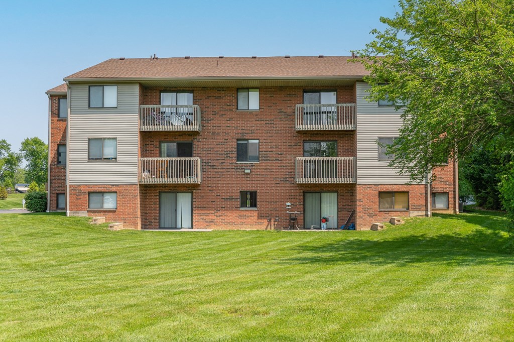 a brick apartment building with balconies and a green lawn