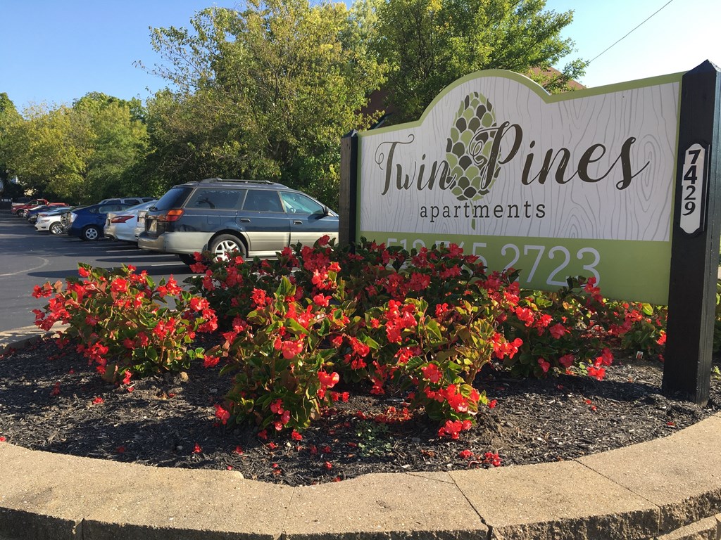 a sign pines apartments in front of red flowers