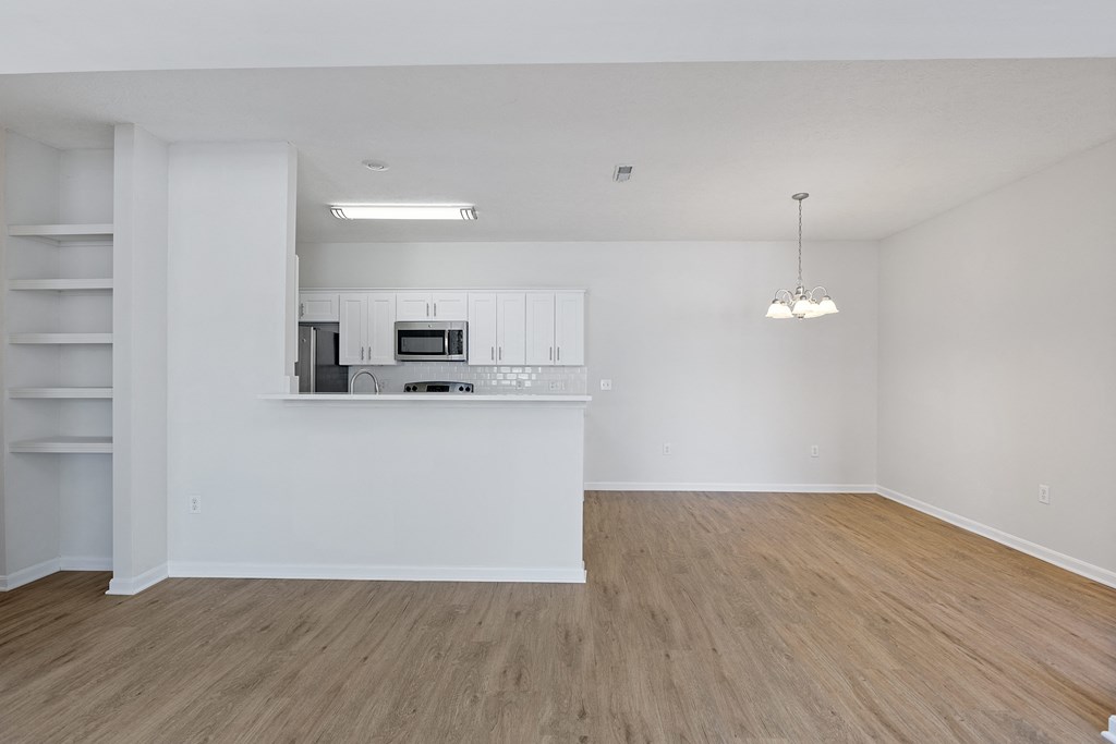 an empty living room and kitchen with white walls and wood flooring