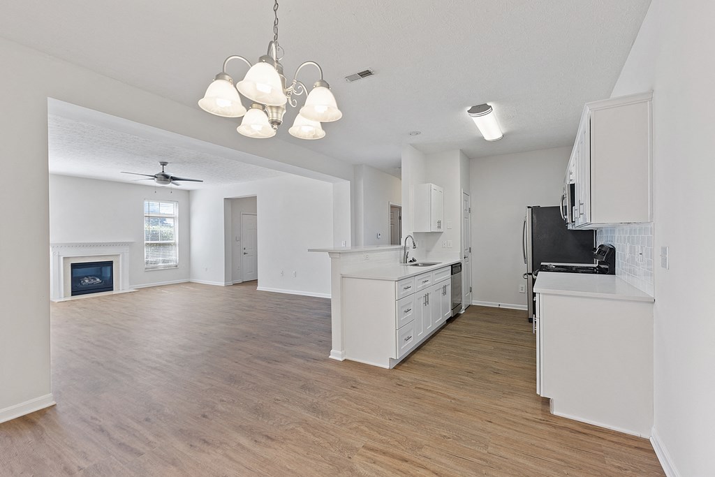 an empty kitchen and living room with white cabinets and a fireplace