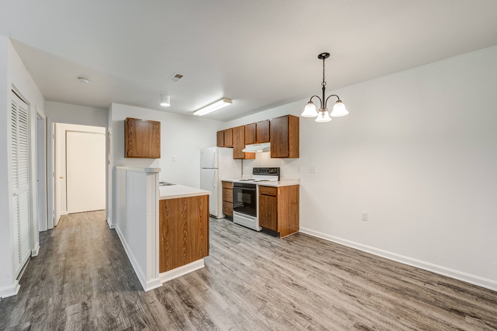 an empty kitchen with wood flooring and white walls and wood cabinets