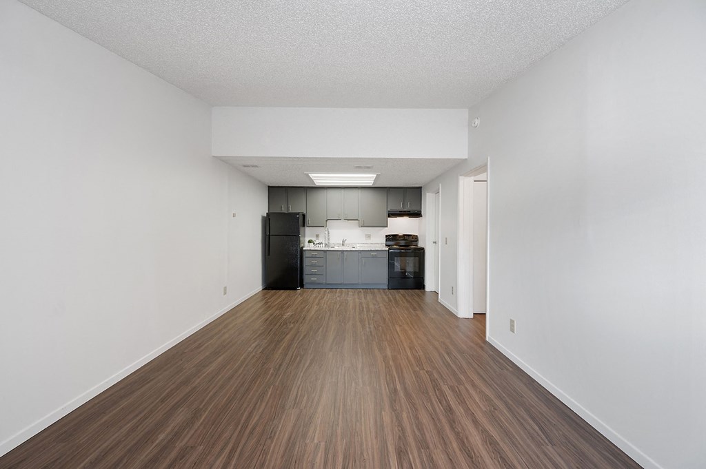 an empty living room and kitchen with white walls and wood floors