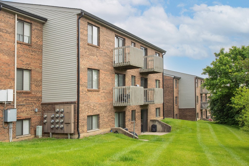 a brick apartment building with balconies and a green yard at The Woodridge Collection, Fairfield, OH 45014