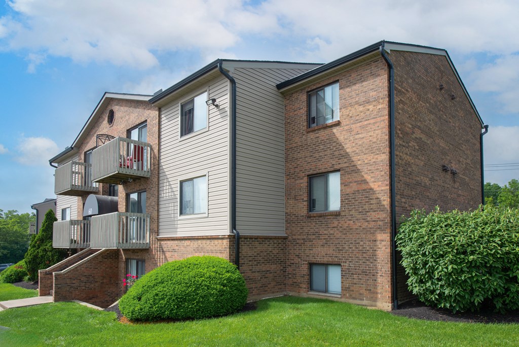 a brick apartment building with two balconies and a green yard at The Woodridge Collection, Fairfield, OH 