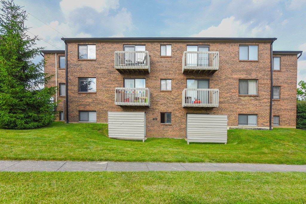 a brick apartment building with three balconies and a green lawn at The Woodridge Collection, Fairfield, Ohio