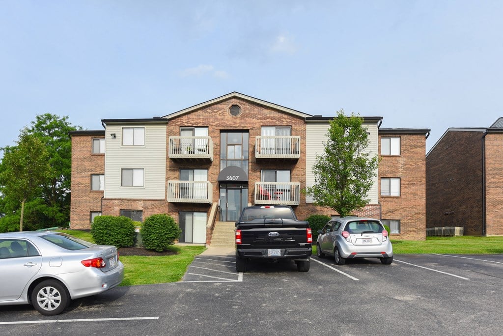 an apartment building with cars parked in a parking lot at The Woodridge Collection, Fairfield, Ohio