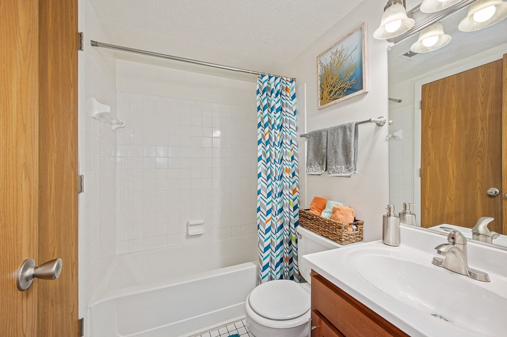 a bathroom with a white bathtub and a white sink with a blue and white shower curtain at The Woodridge Collection, Fairfield Ohio