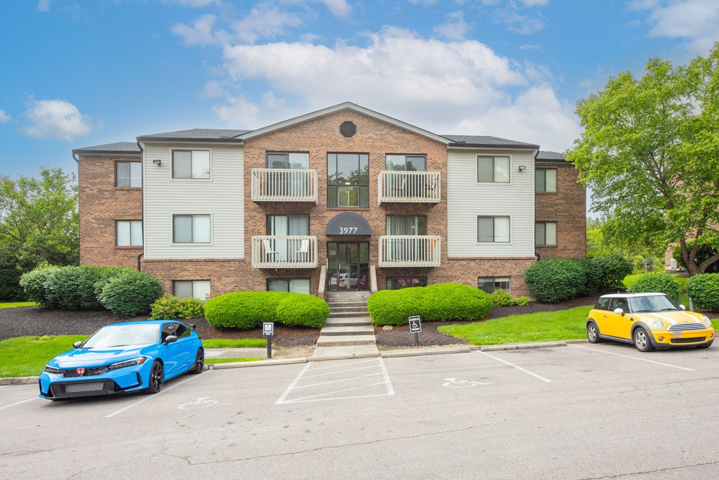 an apartment building with two cars parked in front of it at The Woodridge Collection, Fairfield, Ohio