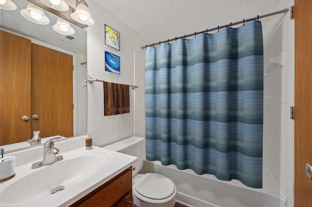 a bathroom with a white sink and a blue shower curtain at The Woodridge Collection, Fairfield, OH 45014