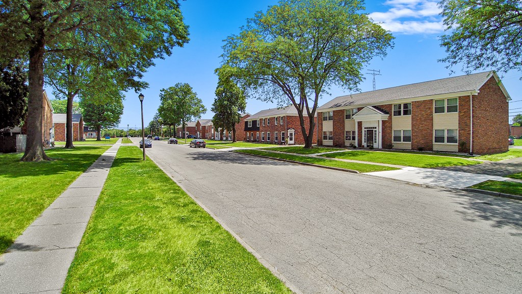 a street in front of a brick building with grass and trees