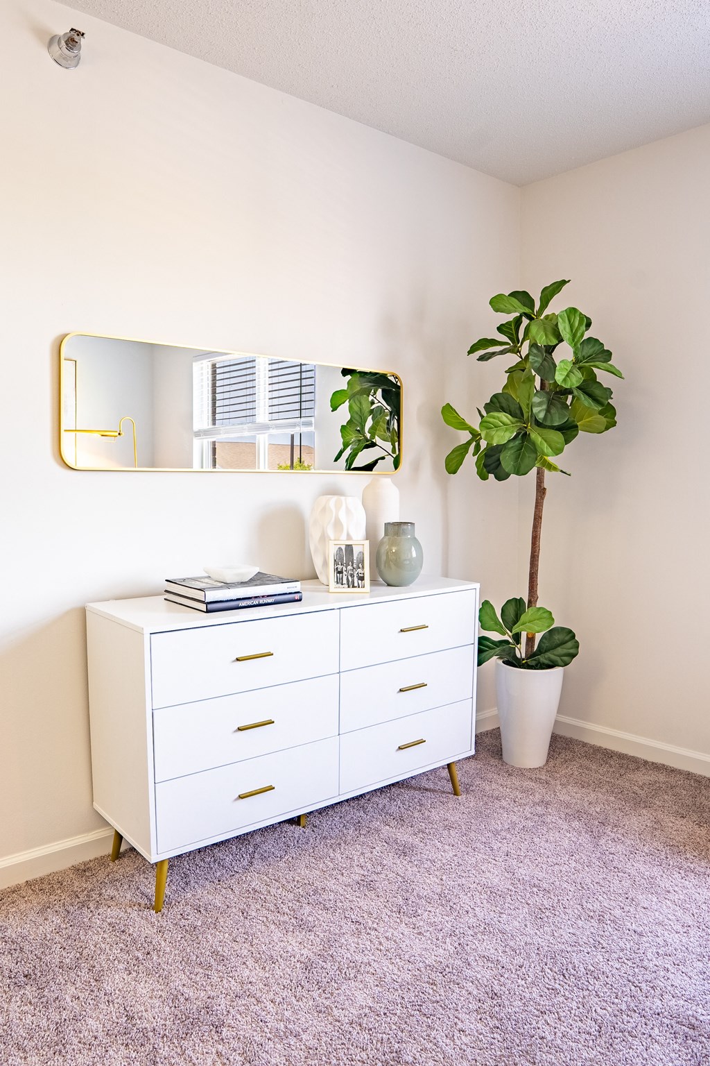 a white dresser with a plant and a mirror in a room