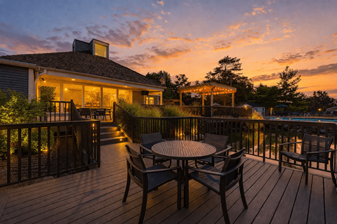 A wooden deck with a table and chairs overlooking a pool.