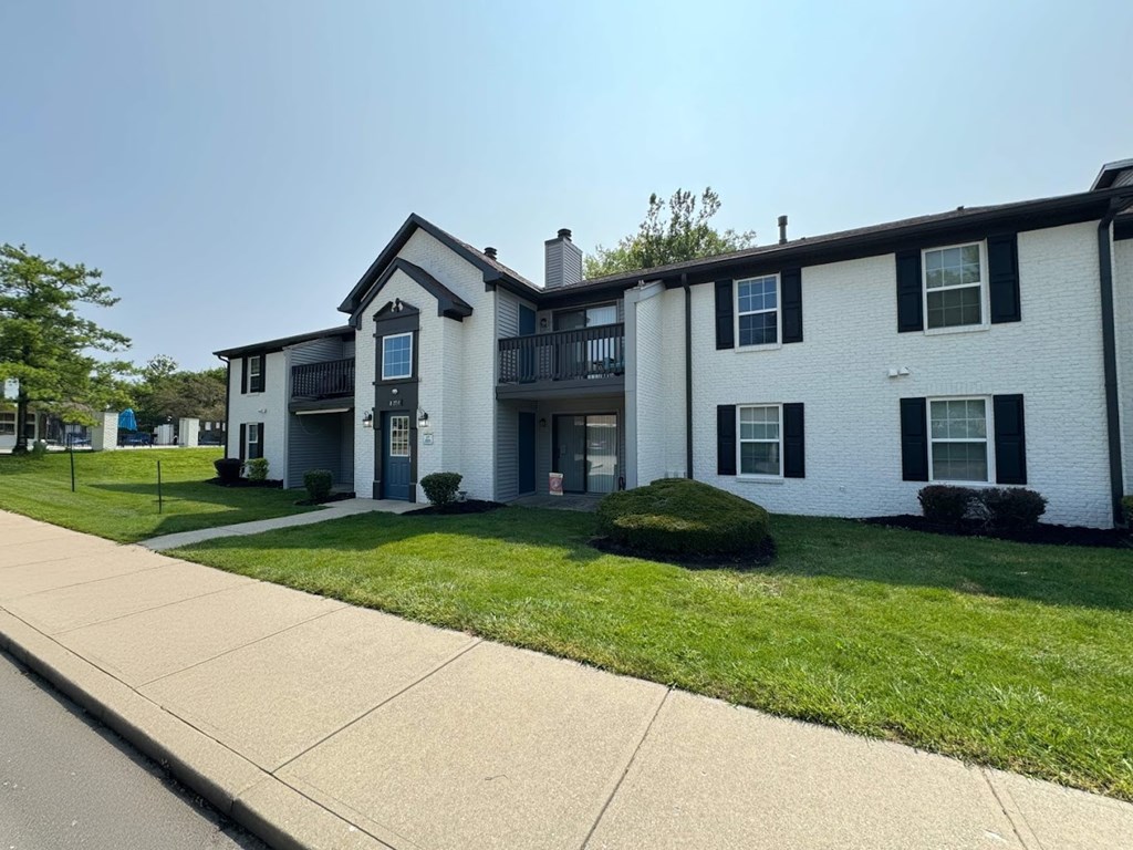 A white two-story apartment building with a black roof and a balcony on the second floor.