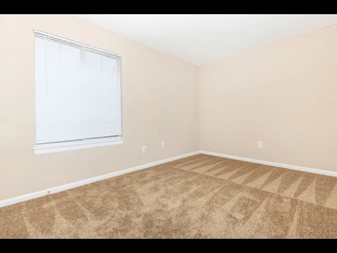 A room with a carpeted floor and a window with blinds.