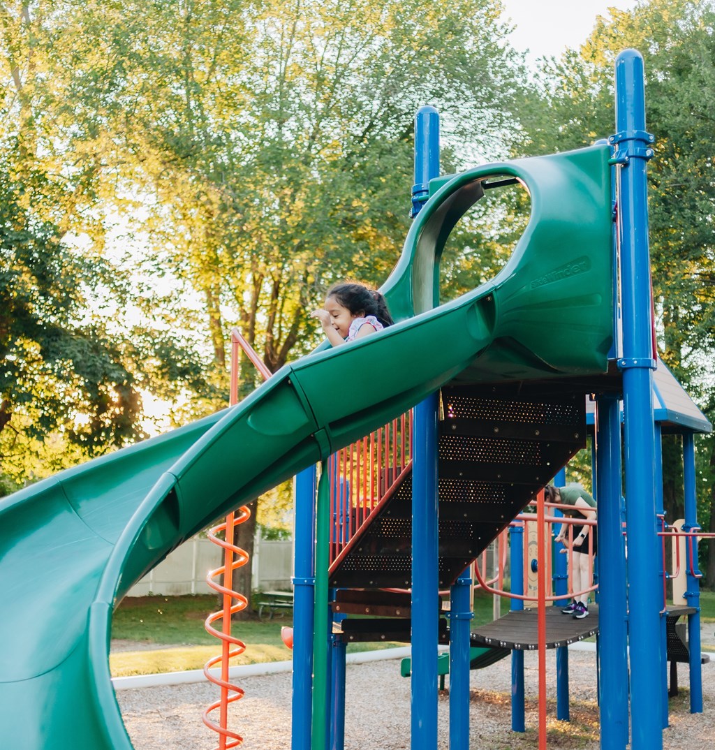 A child slides down a green slide at a playground.