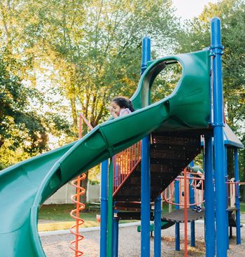 A child slides down a green slide at a playground.