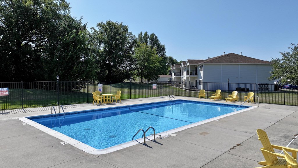 A swimming pool surrounded by yellow chairs and a fence.