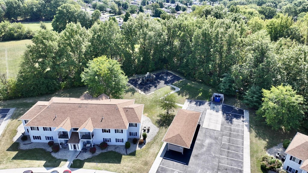 A large white house with a brown roof is surrounded by a parking lot and trees.